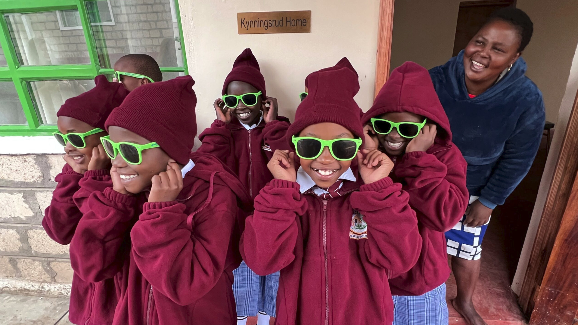 A group of kenyan children with read hoodies and green sunglasses
